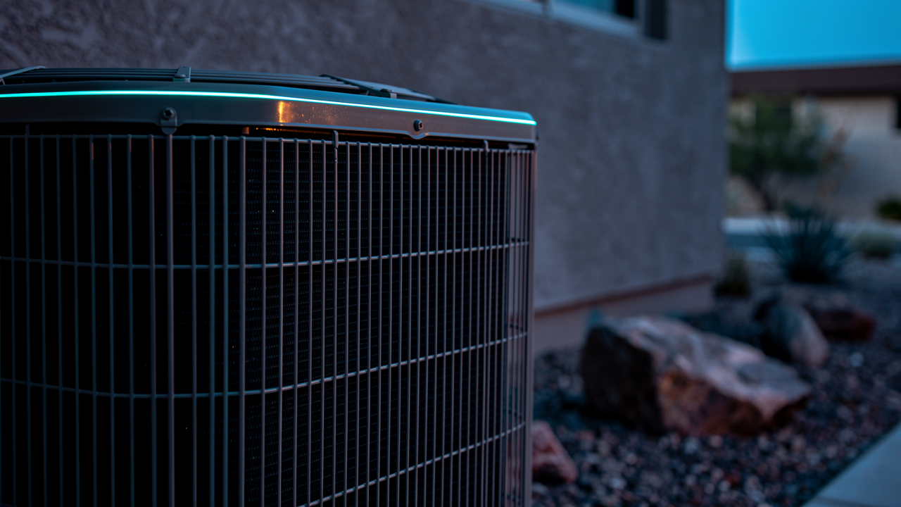 A residential AC condenser unit beside a Phoenix home at dusk, lit with cool blue light